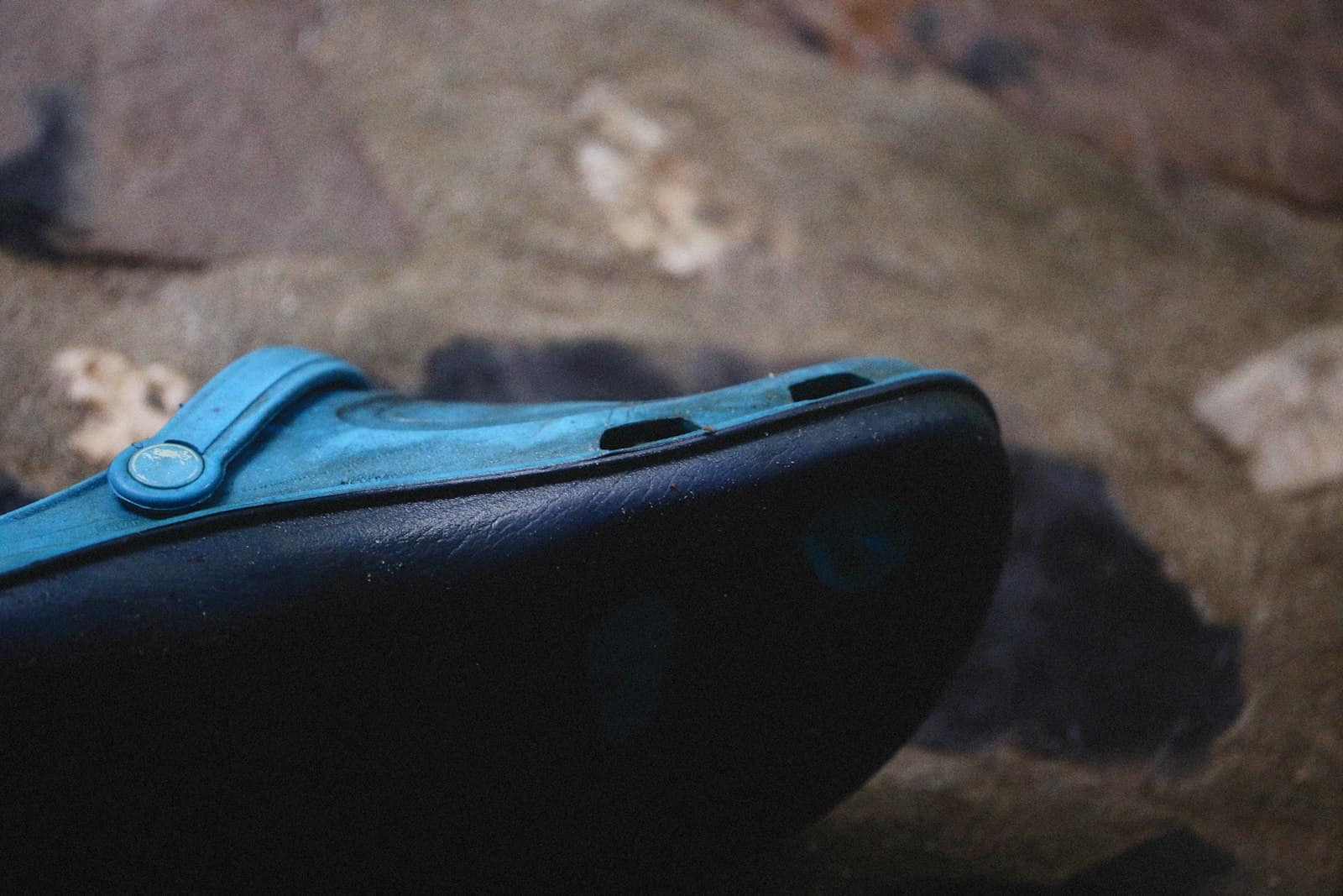 A moulded foam shoe in blue resting on a rock, the rounded sole wall catching the light
