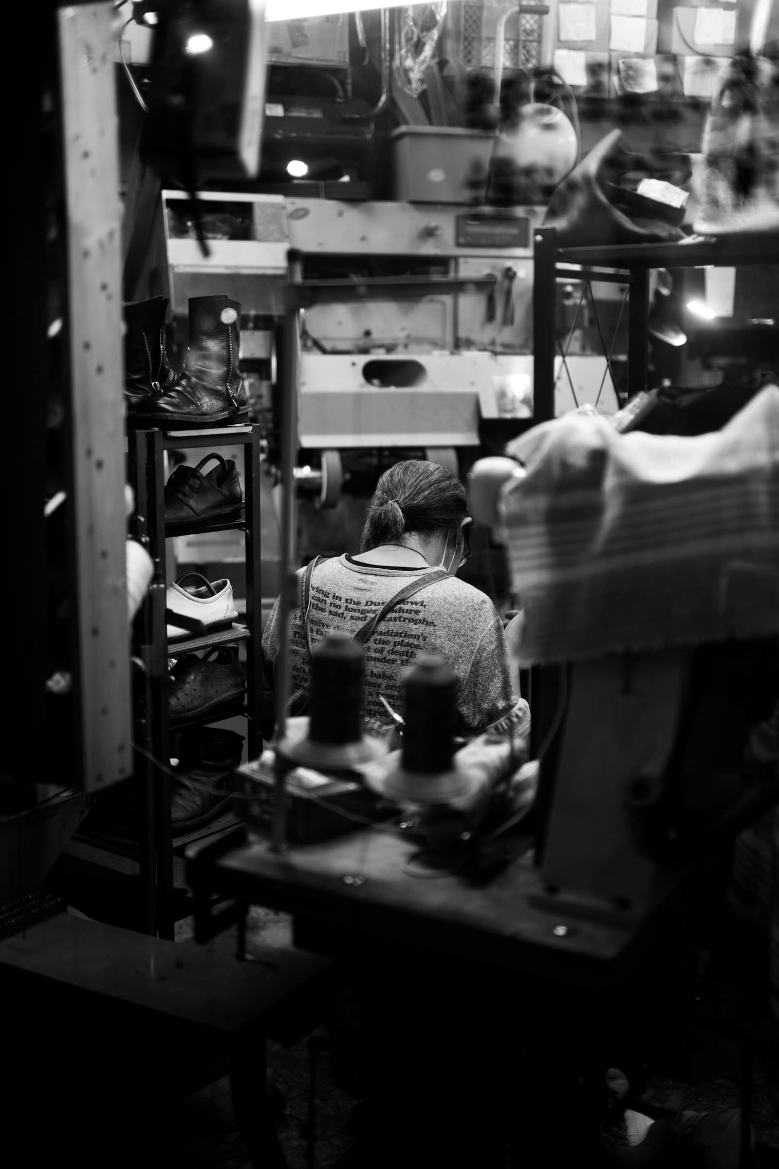 An operator at her machine on a shoe production line, finished pairs racked beside her